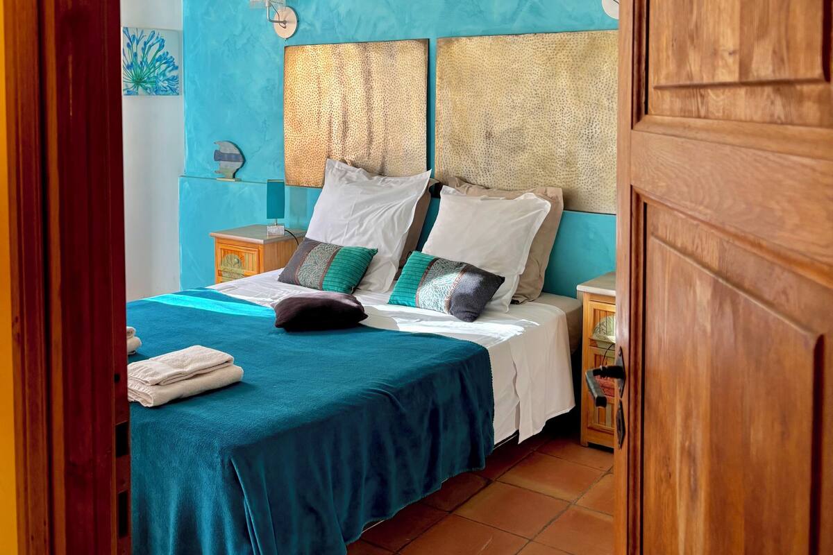 Une chambre à coucher avec un lit, des oreillers, une table de chevet, une horloge murale et une porte.