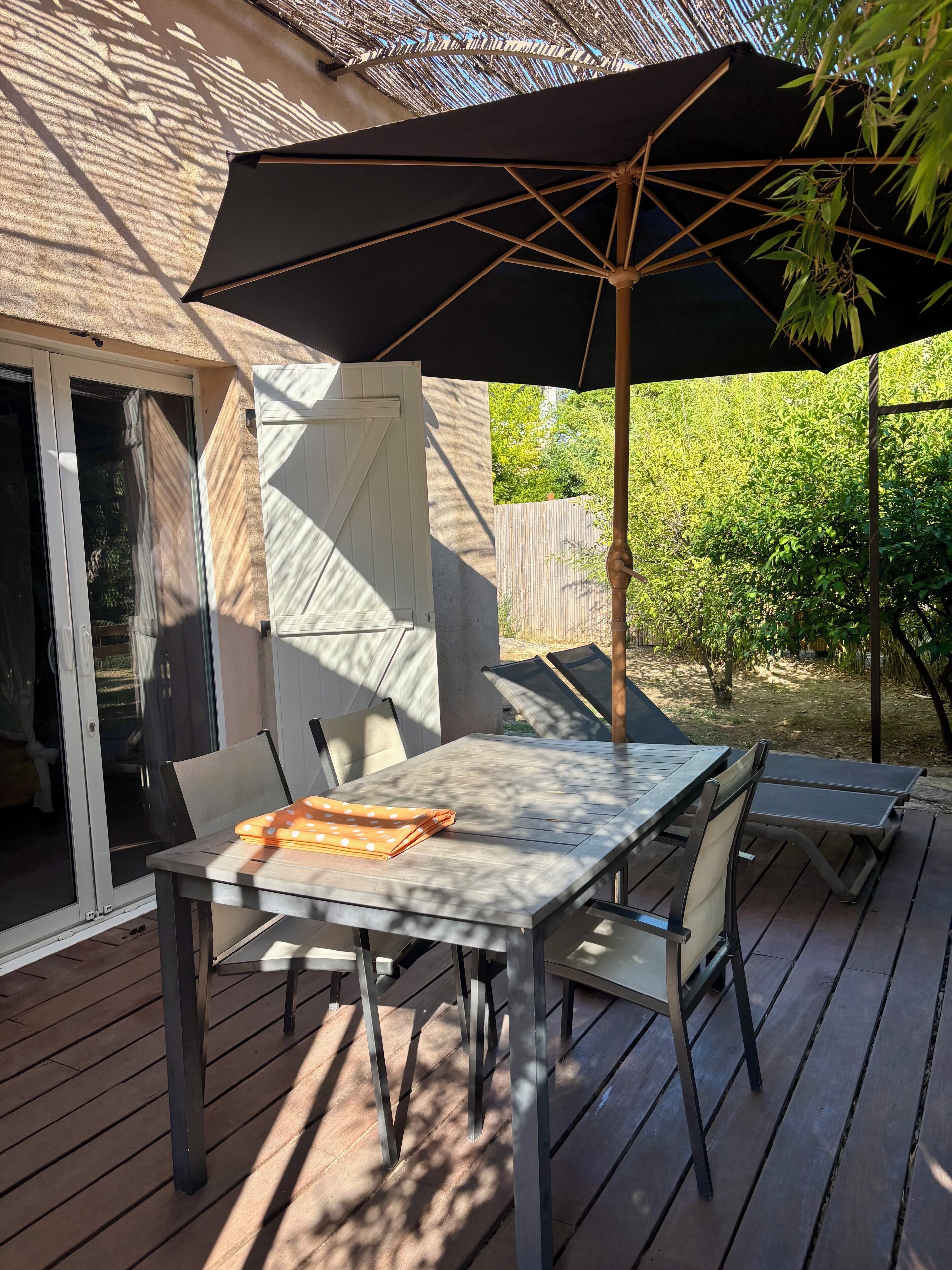 An outdoor patio with a table and chairs, a large umbrella, and a view of a garden.