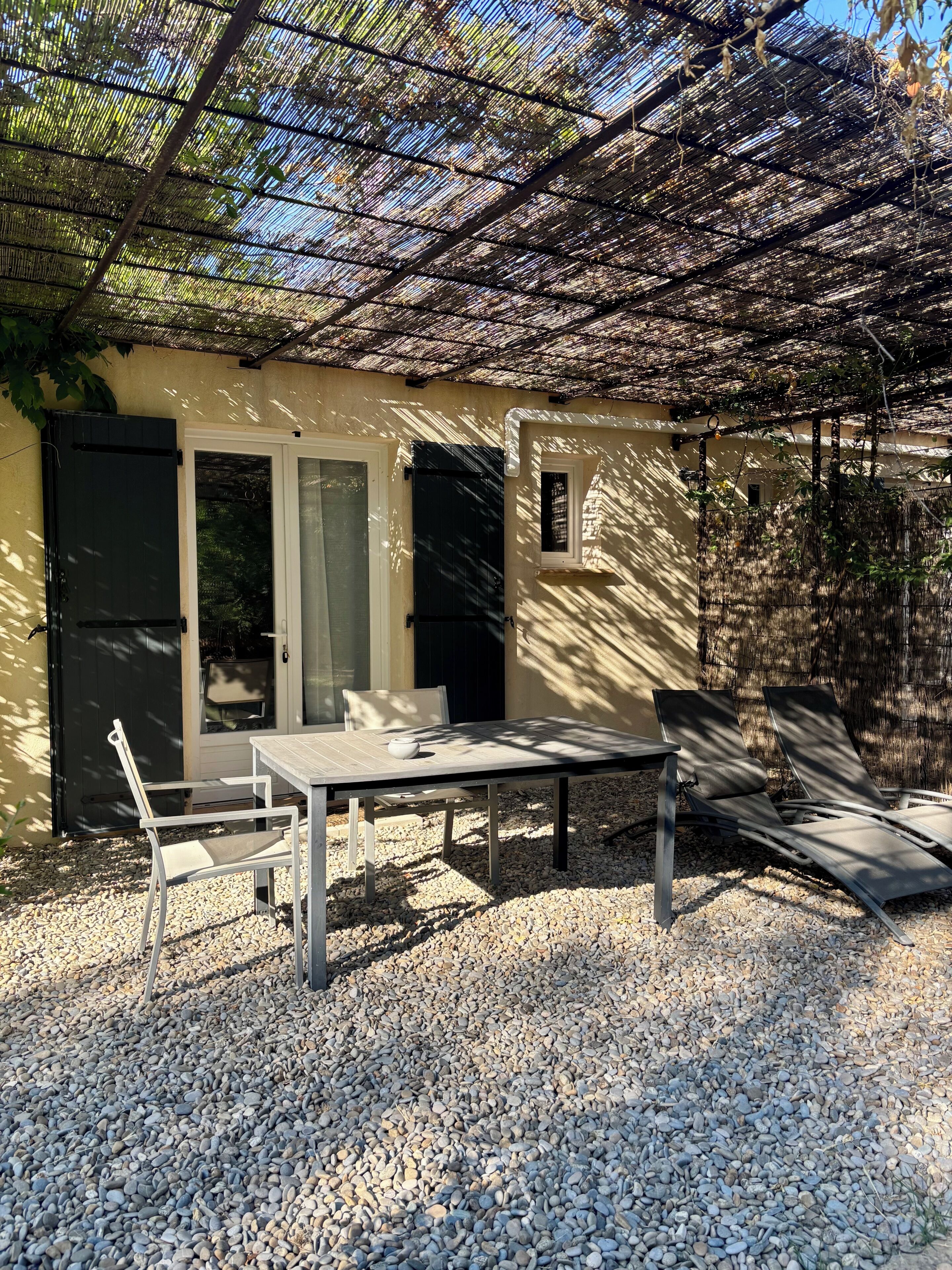 An outdoor patio with a table and chairs, a pergola overhead, and a door leading to a covered area.