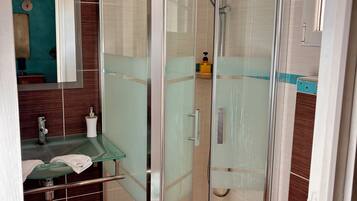 Een badkamer met een douche met glazen wanden, een wastafel met een glazen blad en een spiegel boven de wastafel.