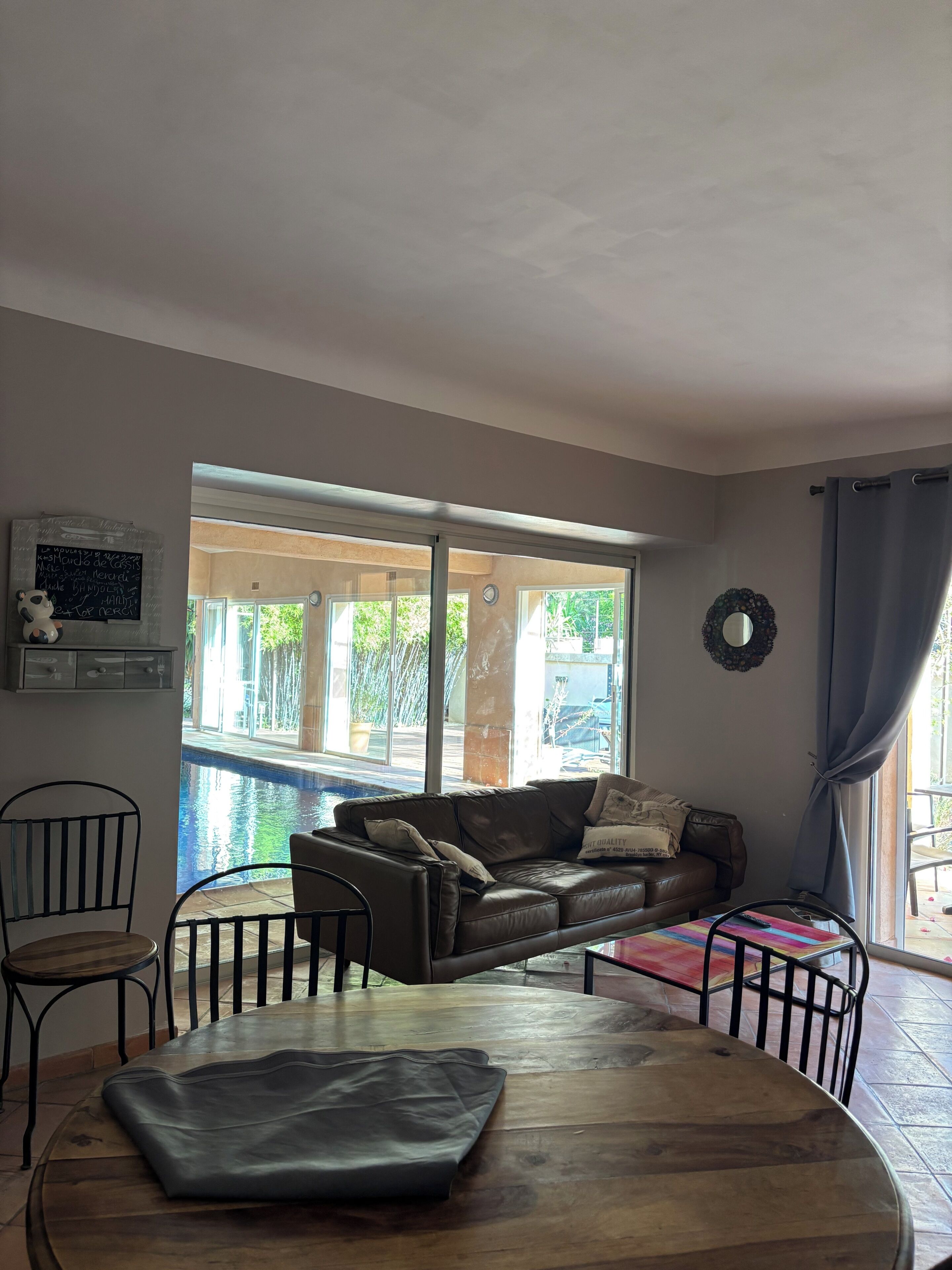 A living room with a sofa, chairs, a wooden table, a pool view, and a large window.