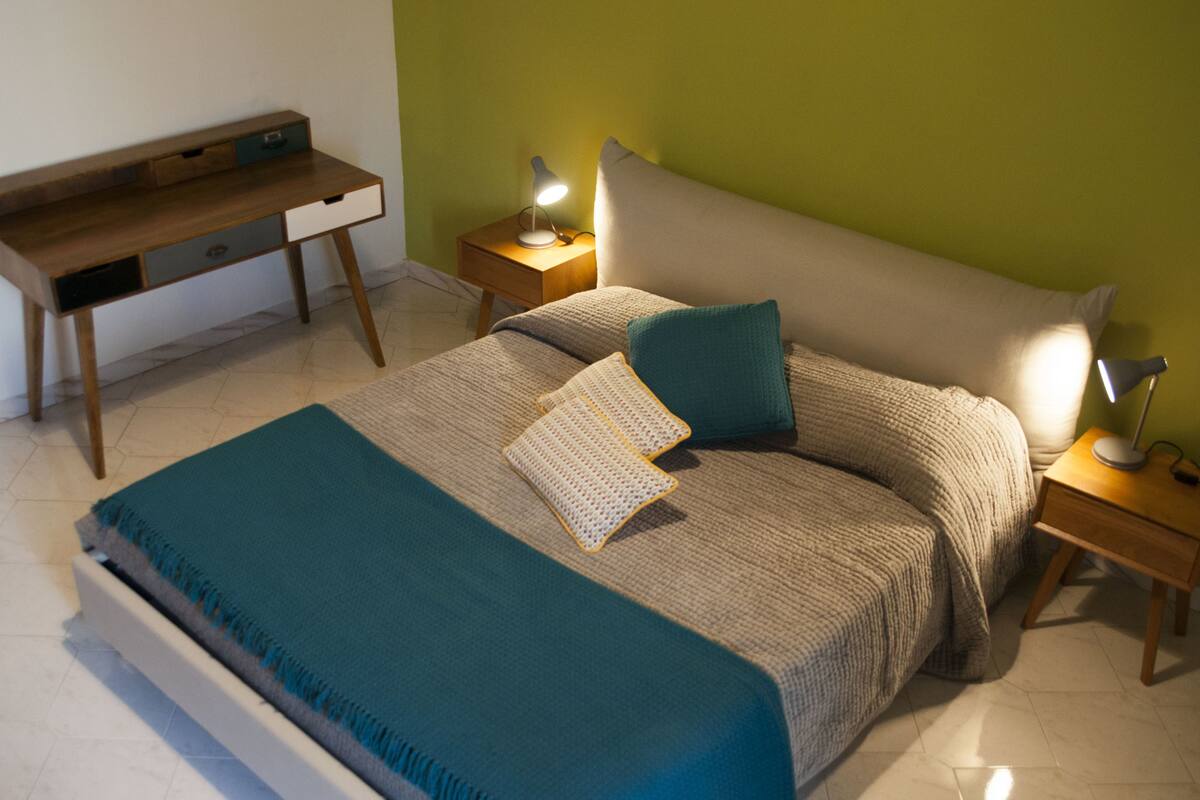 Une chambre à coucher avec un lit, des tables de chevet, un bureau et une lampe.