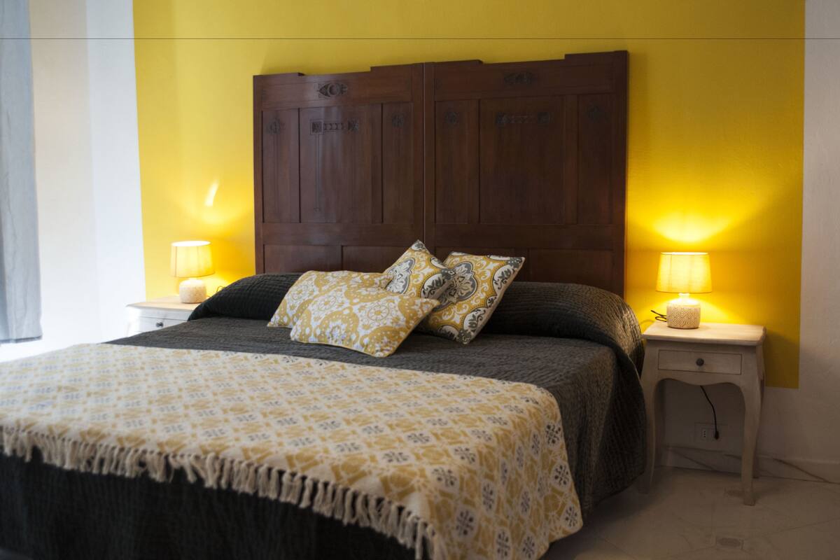 Un lit avec une couvre-lit à motifs, deux oreillers et une tête de lit en bois. Il y a deux tables de chevet avec des lampes.