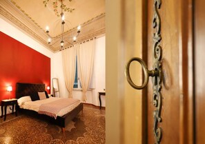A bedroom with a large bed, a chandelier, and a red accent wall. - B&B Retrò (Pisa)