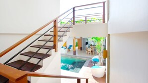 A modern interior with a staircase leading to a balcony, a pool area, and a dining space. - Apple Villa and Apartment (Kerobokan)