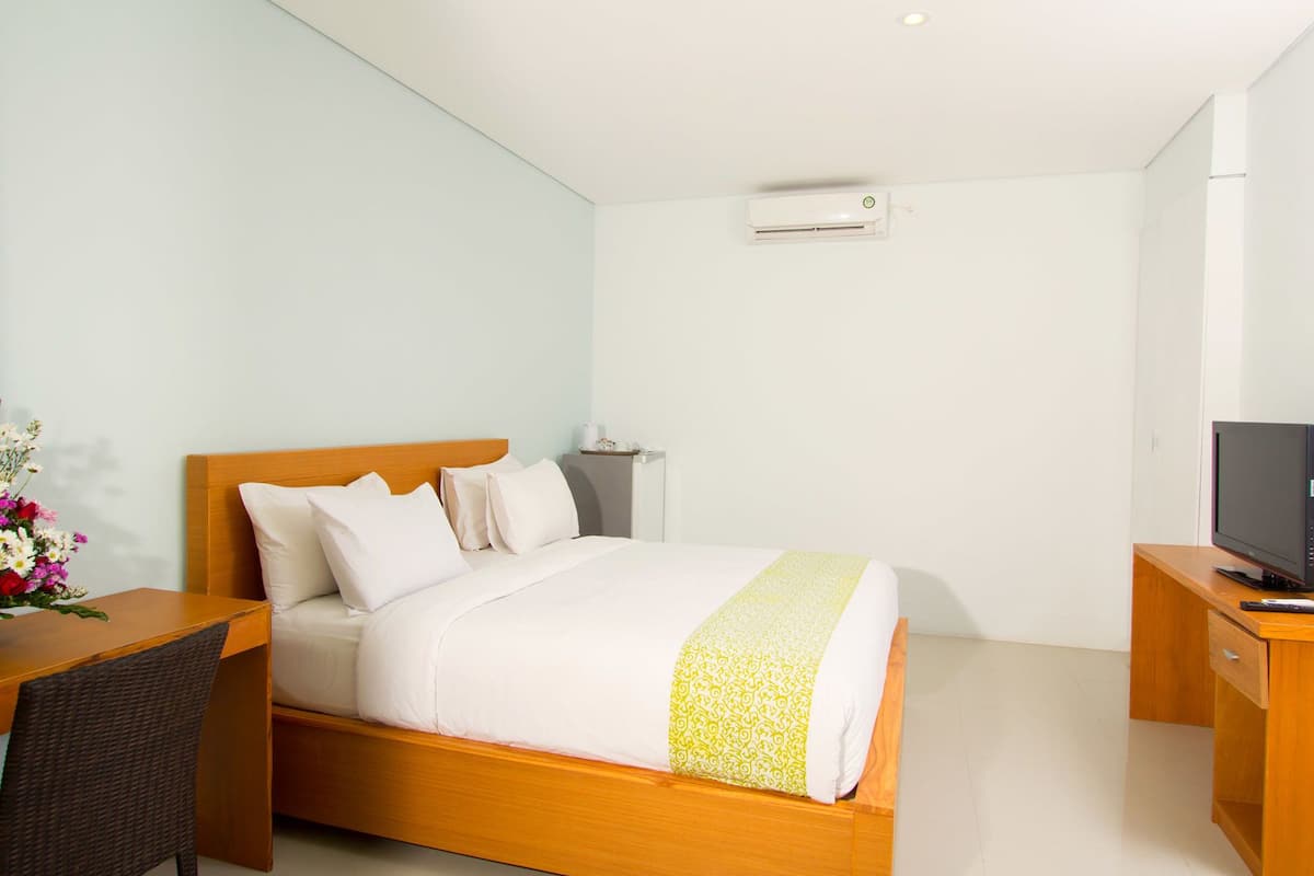 A hotel room with a wooden bed, a desk with a chair, a television, and an air conditioning unit on the wall.