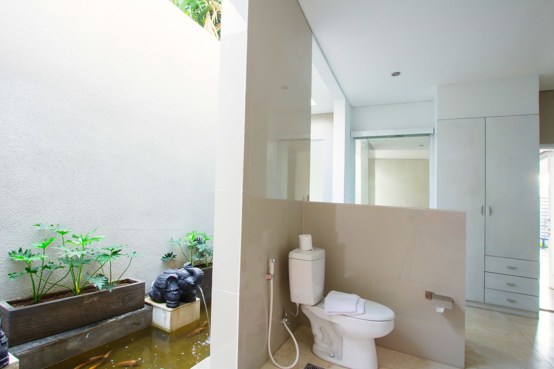 Ein modernes Badezimmer mit Toilette, Bidet und einem kleinen Gartenbereich mit Pflanzen und einem Wasserspiel.