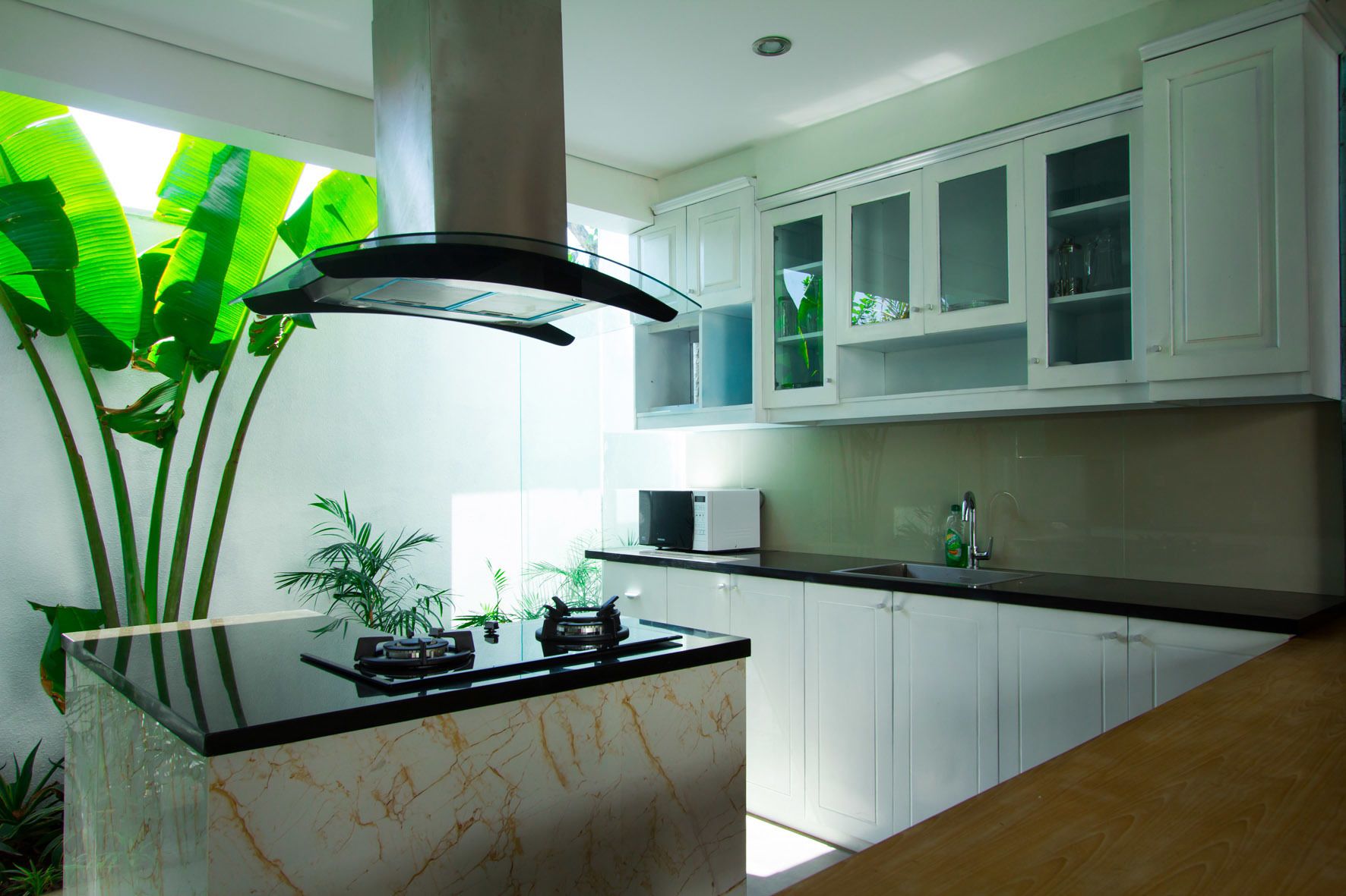 Una cocina moderna con una isla central, armarios blancos y un amplio ventanal con follaje verde.