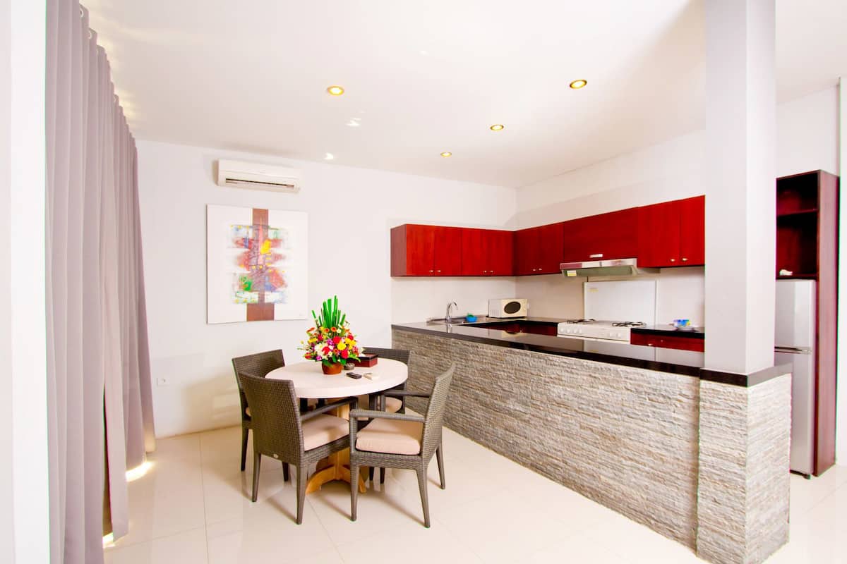 A modern kitchen with red cabinets, a central island, and a dining area with wicker chairs.