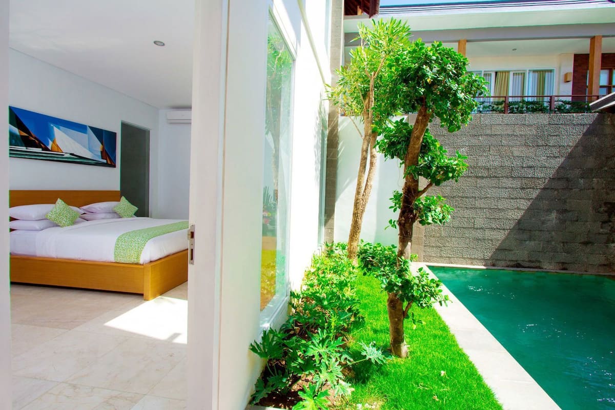 A modern hotel room with a bed, a view of a swimming pool, and a staircase leading to an upper level.