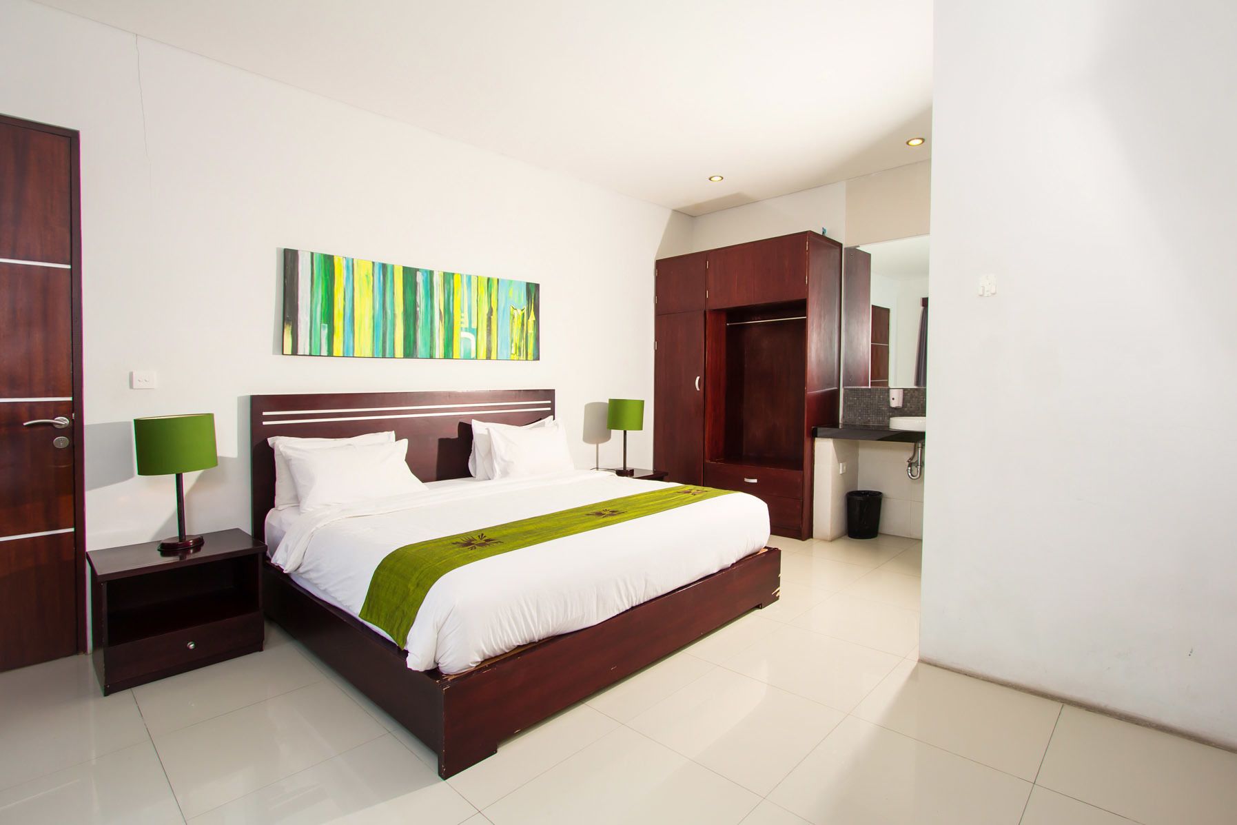 A hotel room with a large bed, two bedside tables with lamps, a wardrobe, and a bathroom visible through an open door.