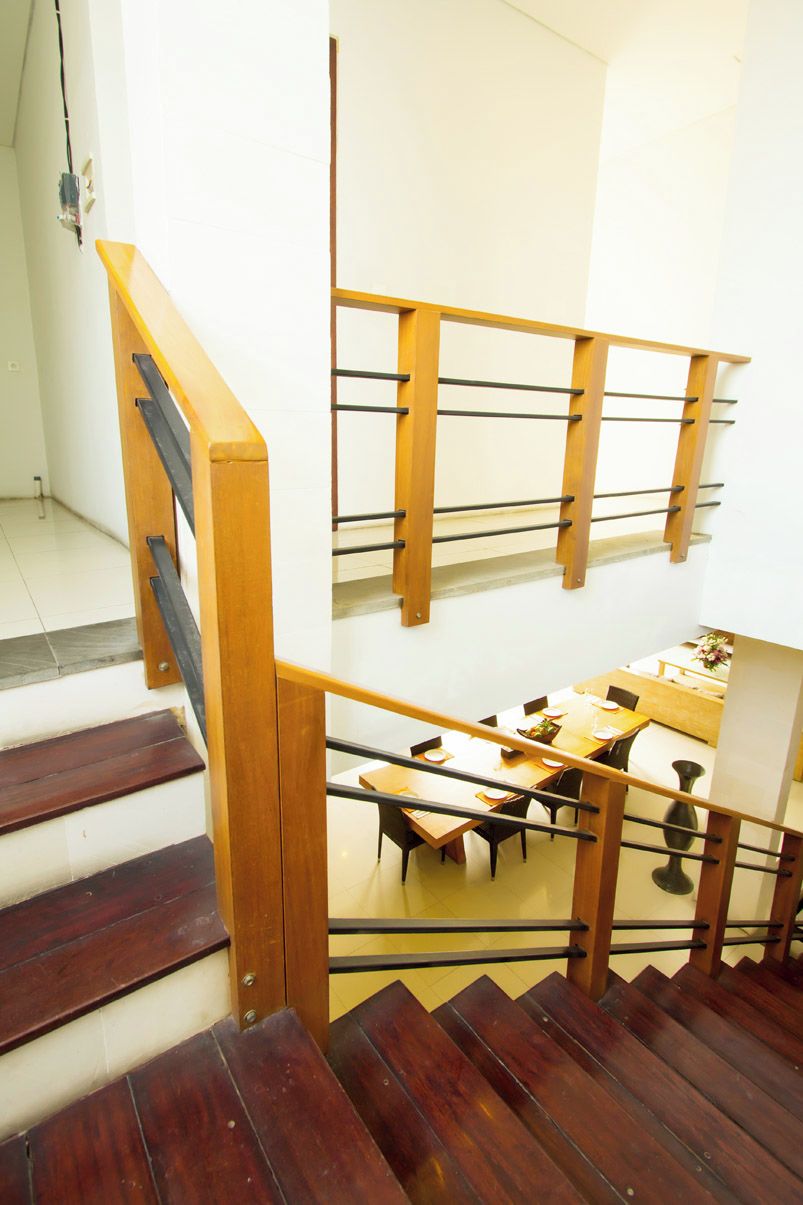 Un escalier en bois, doté d’une rampe en verre, mène à un espace repas aménagé avec des tables et des chaises.