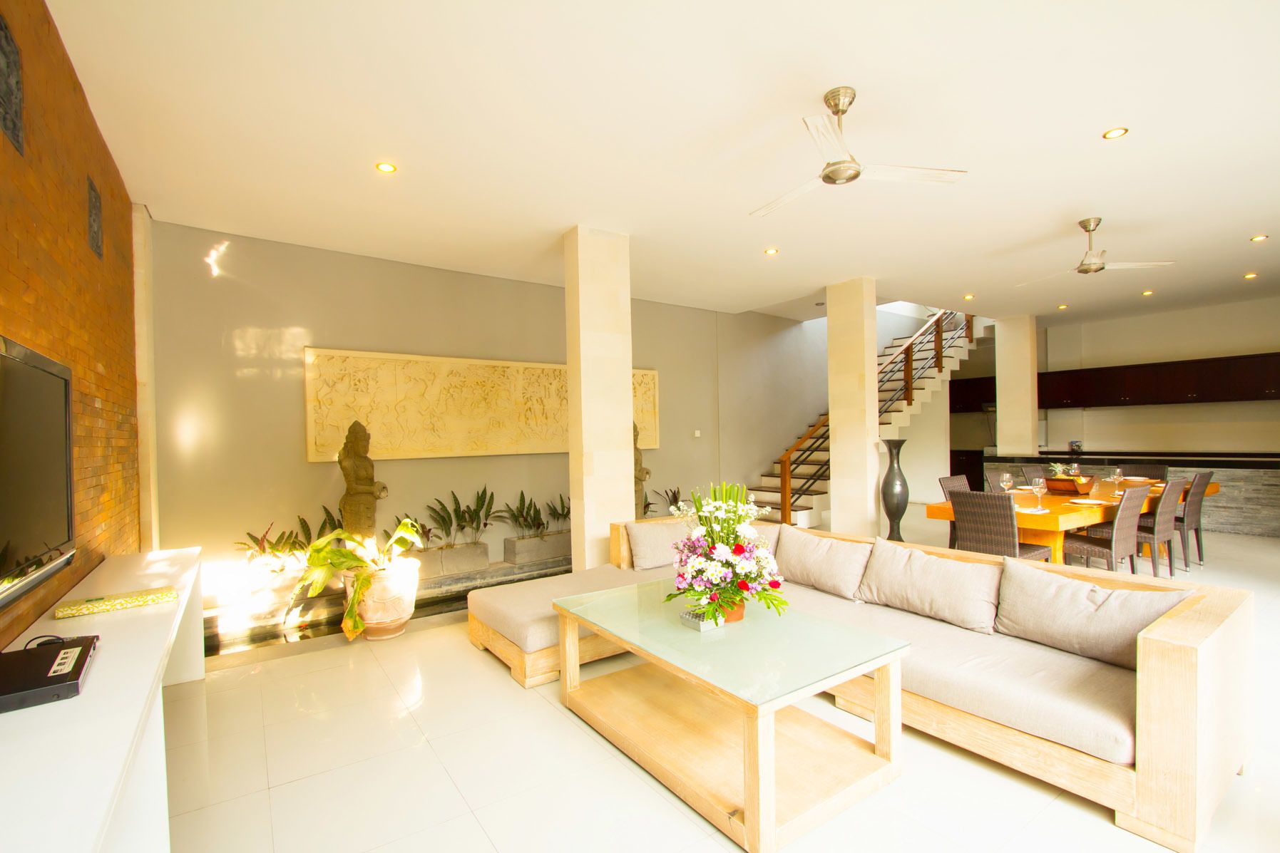 A modern living room with a sofa, coffee table, and decorative plants. There is a staircase leading to an upper level.