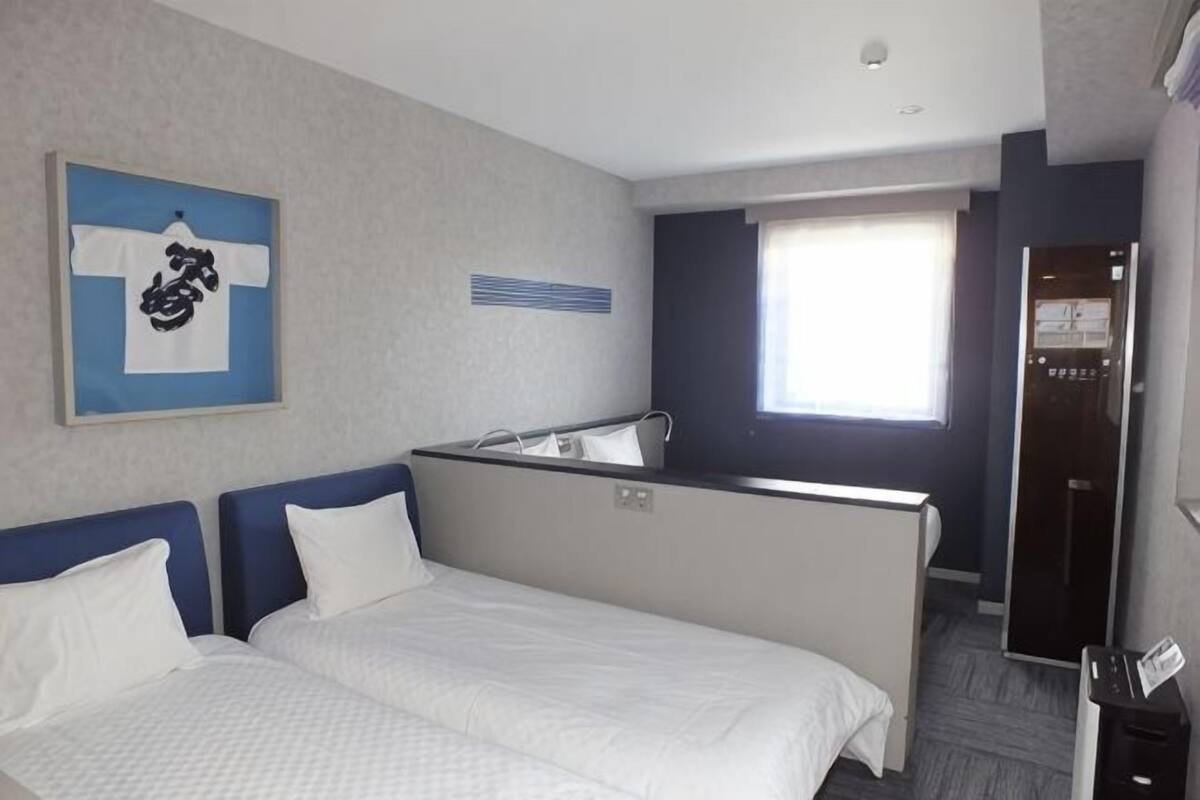 Ein Hotelzimmer mit einem Bett, einer kleinen Küchenzeile, einem Spiegel und einem Fenster.