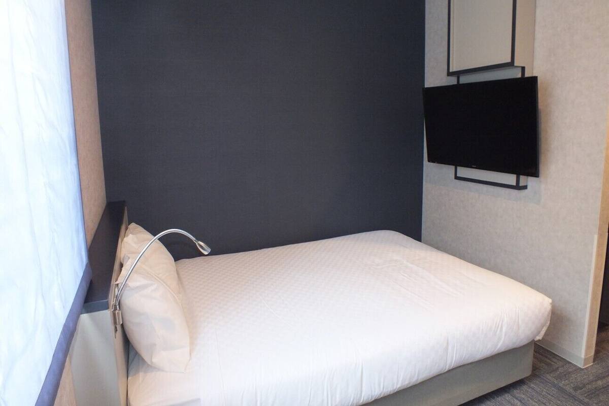 Ein kleines, modernes Schlafzimmer mit einem Einzelbett, einem dunklen Kopfteil, einem flachbildfernseher an der Wand und einem Nachttisch mit Lampe.