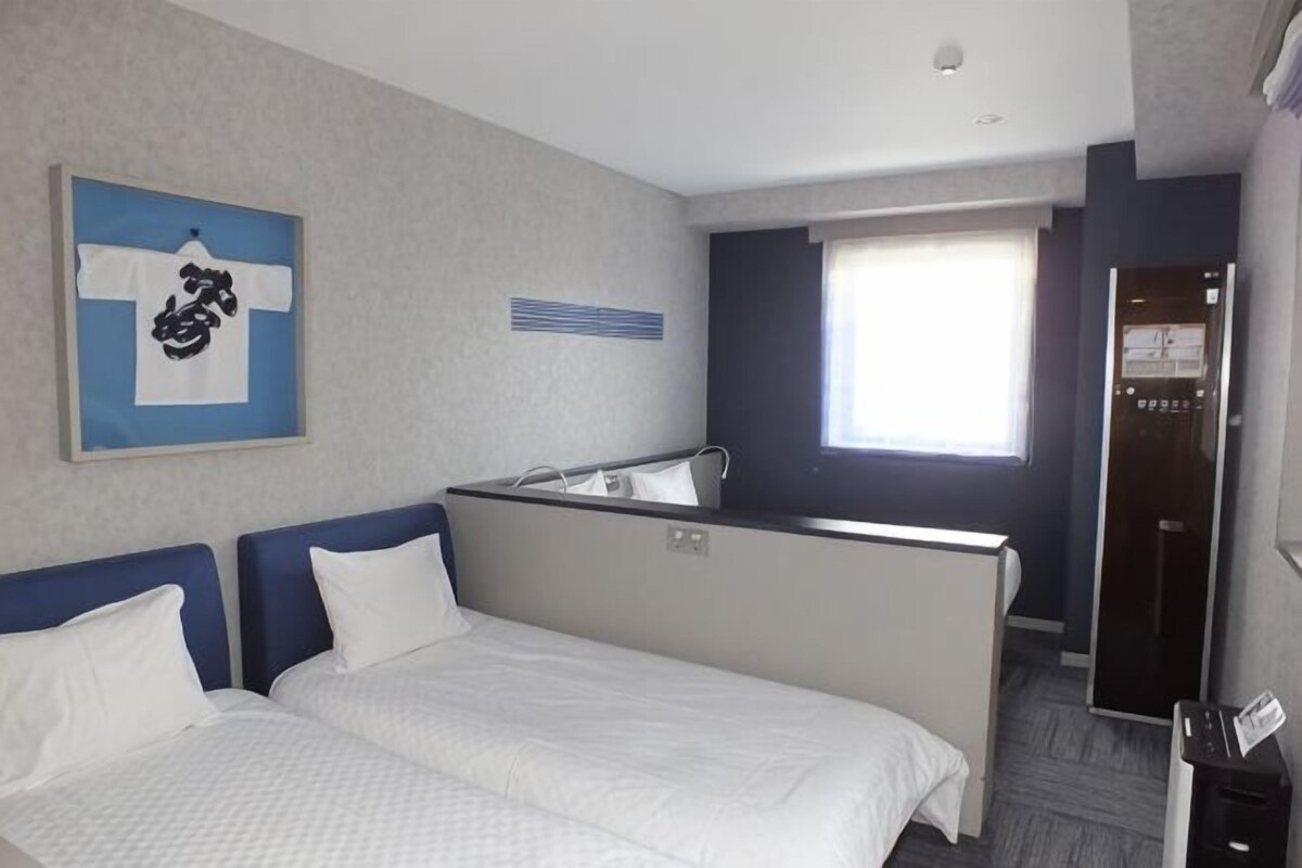 A hotel room with a bed, a small kitchenette, a mirror, and a window.