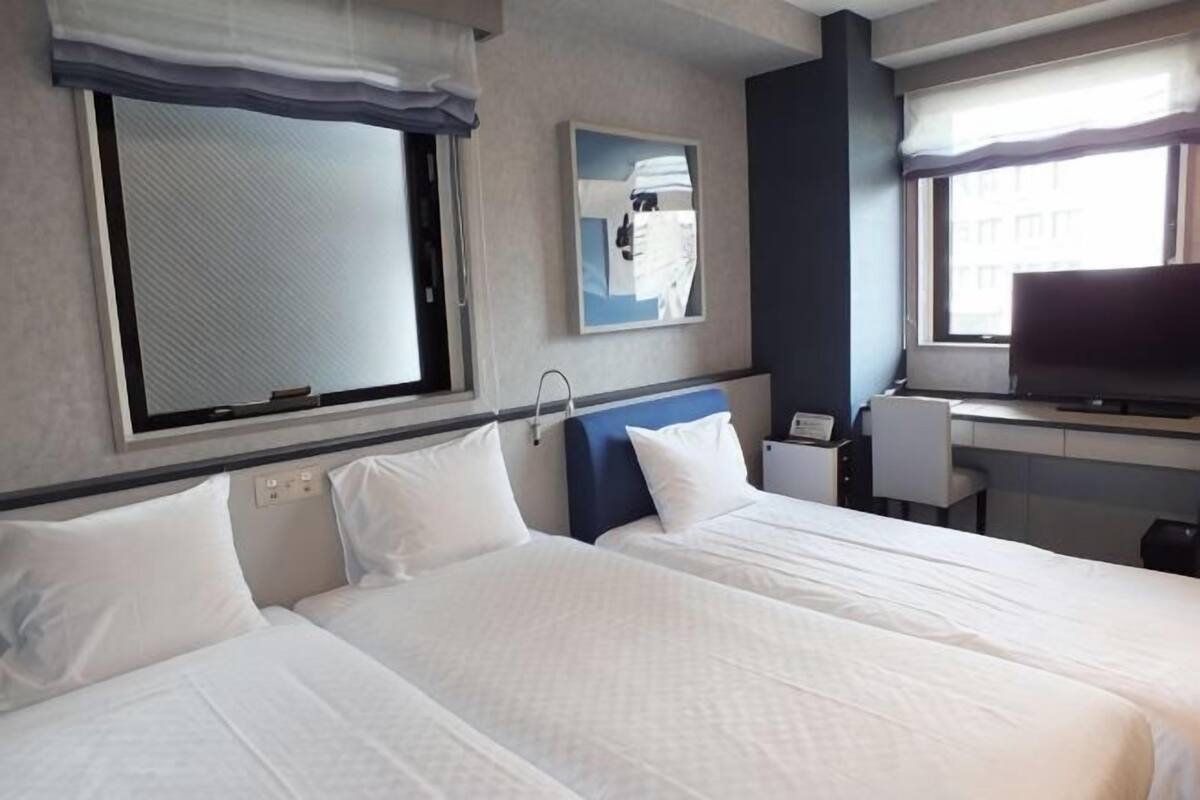 Ein Hotelzimmer mit zwei Betten, einem Schreibtisch, einem Fernseher und einem fenster mit Vorhängen.