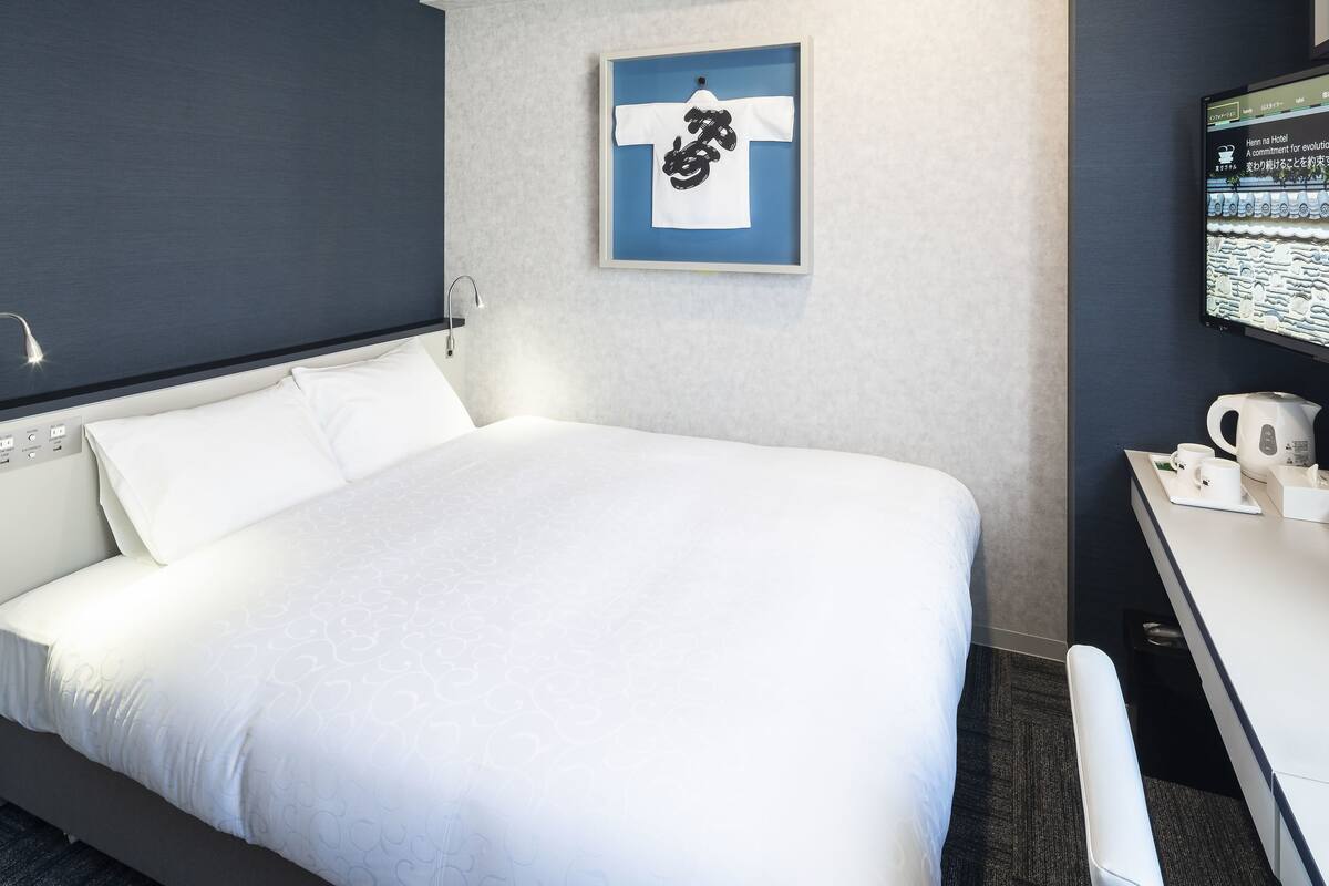 Ein Hotelzimmer mit einem Bett, einem Schreibtisch mit Computer und einem gerahmten Kunstwerk an der Wand.
