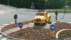 En rondell med vägvisningsskyltar, en gul bil som är dekorerad med blommor och en skylt som visar ”ANTICO TRE VALLI” och ”Via Torino”.