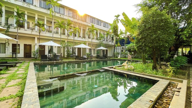 A pool area with lounge chairs and umbrellas, surrounded by a building with balconies and plants. - WORLD WALKERs - Hostel (Siem Reap)