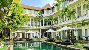 A hotel courtyard with a swimming pool, lounge chairs, umbrellas, and a multi-story building with balconies. - WORLD WALKERs - Hostel (Siem Reap)