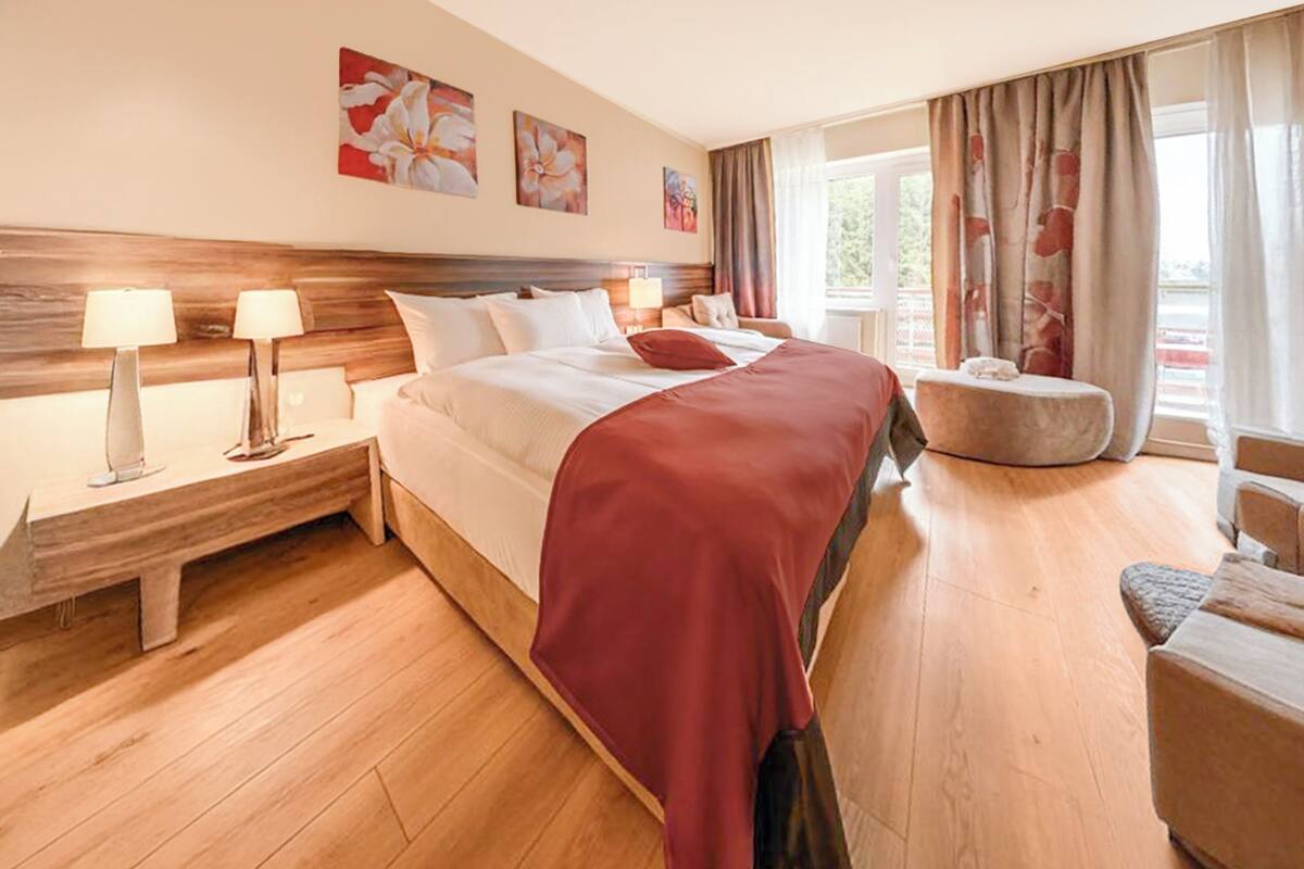 Une chambre d’hôtel avec un grand lit, deux tables de chevet avec des lampes, une petite table ronde et une fenêtre avec des rideaux.