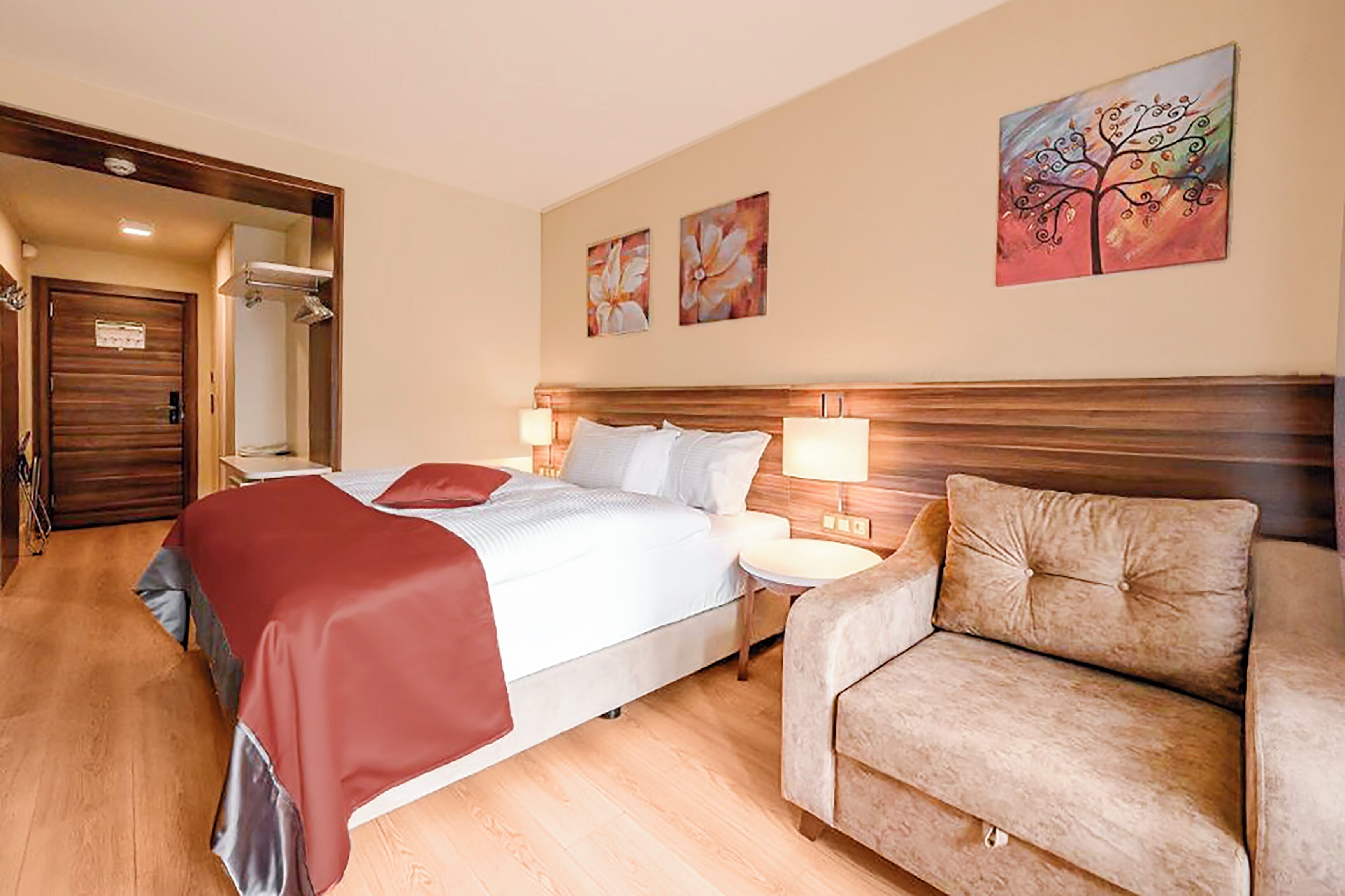 A hotel room with a bed, bedside tables, a sofa, and artwork on the wall.