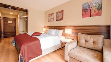A hotel room with a bed, bedside tables, a sofa, and artwork on the wall.