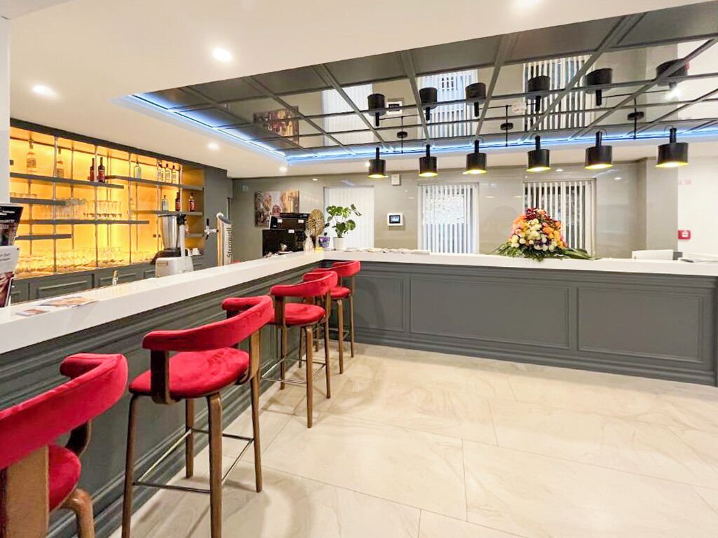 Een moderne bar met een lange toonbank, rode barkrukken en een decoratieve bloemstelling.