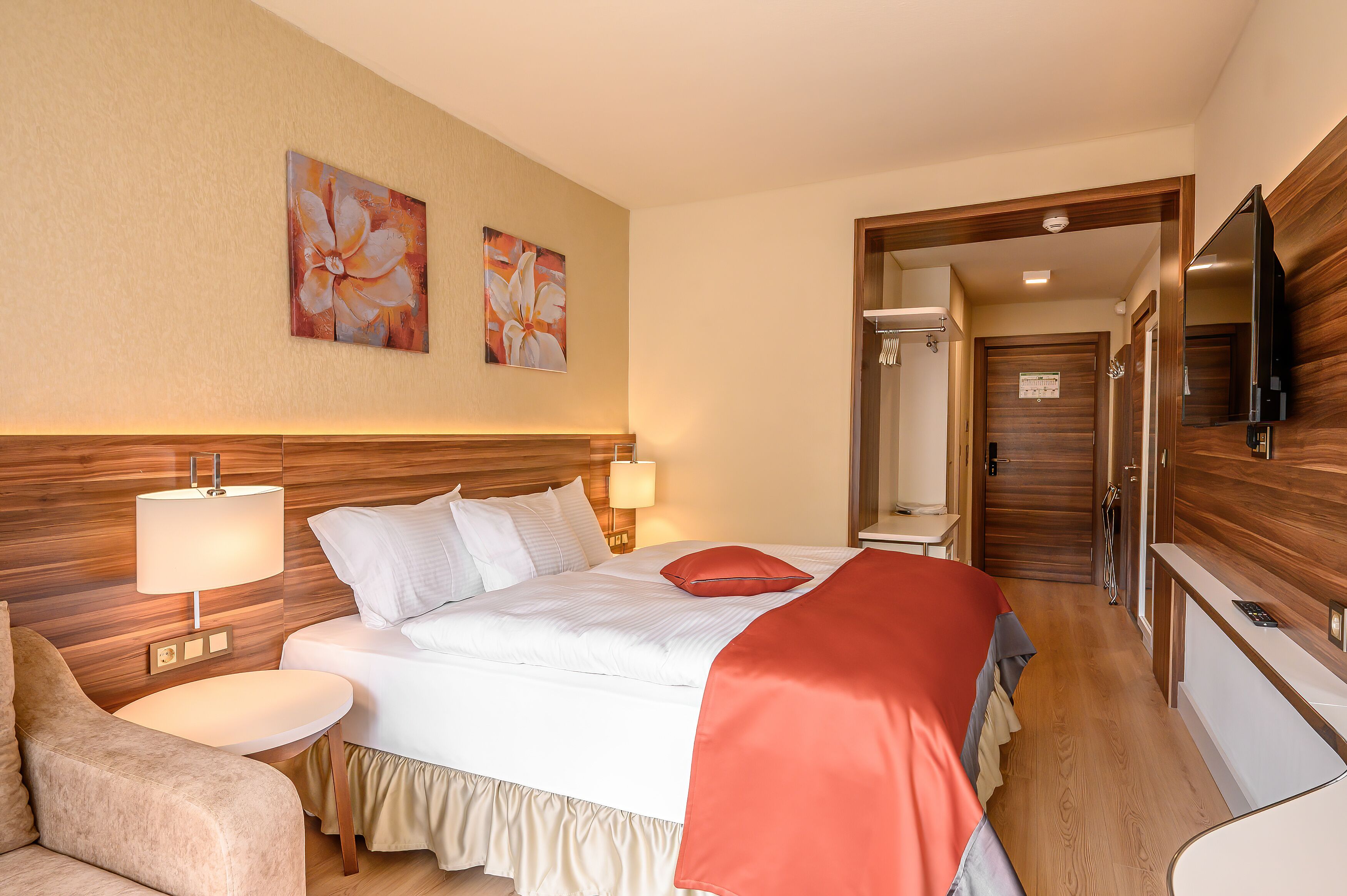 A hotel room with a large bed, two bedside lamps, a flat-screen TV, and a wooden headboard.