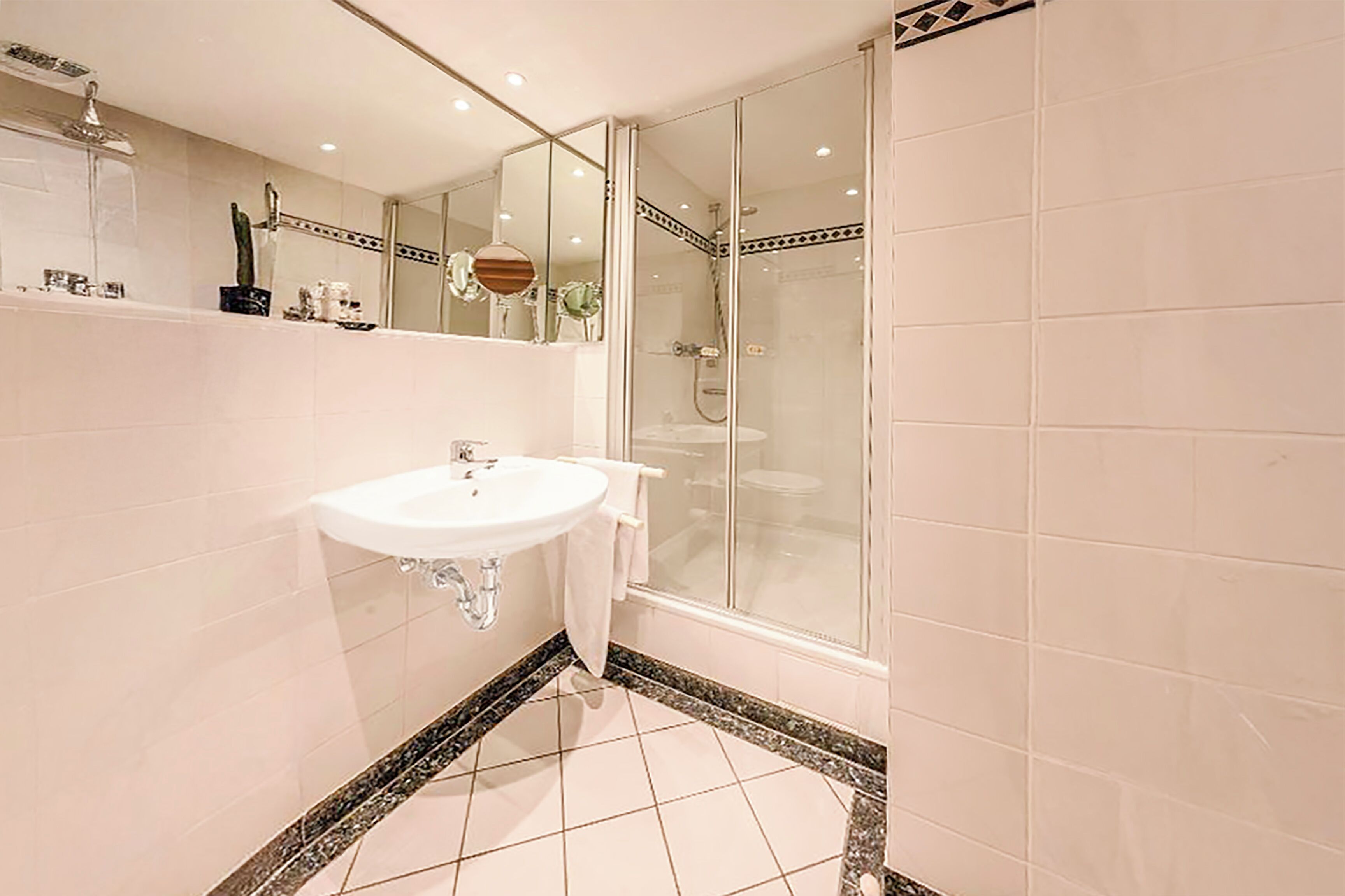 Ein modernes Badezimmer mit einem weißen Waschbecken, einem Spiegel und einer Glasdusche.
