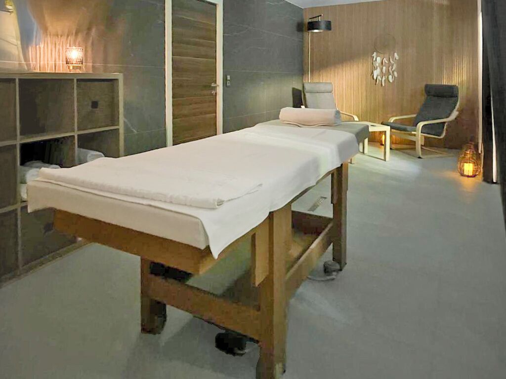 A treatment room with a wooden table, a chair, and a small table with a lamp.