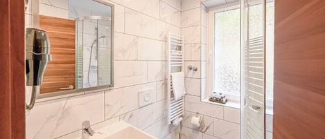 Un baño moderno con lavamanos de mármol, cabina de ducha de vidrio y toallero empotrado.
