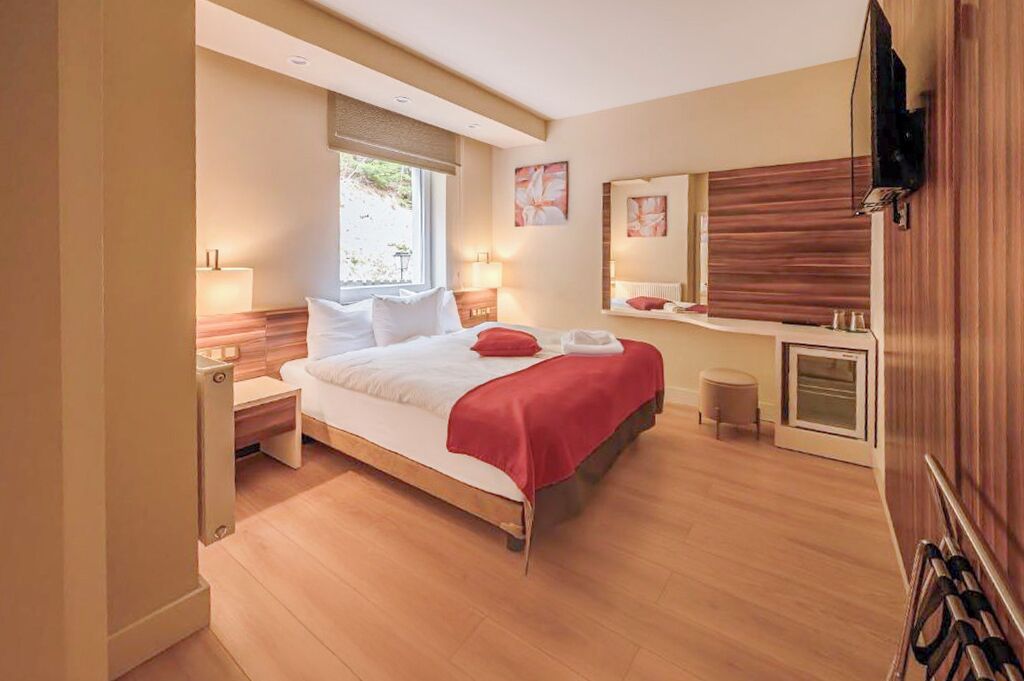 Una habitación de hotel moderna con una cama de madera, mesitas de noche, un espejo grande y una ventana pequeña.
