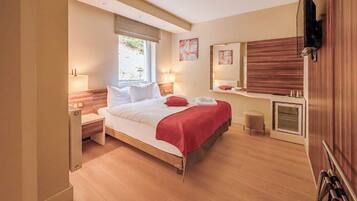 Una habitación de hotel moderna con una cama de madera, mesitas de noche, un espejo grande y una ventana pequeña.
