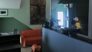 A room with a green wall, a wooden door, a desk with a laptop, an orange chair, and a large window with a view of the outside. - B&B Minicurcu (Acireale)