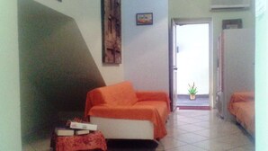 A small, well-lit room with a sofa, a small table with books, and a potted plant. - B&B Minicurcu (Acireale)