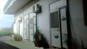 A building with three doors, each with a window and a small air conditioning unit above. There are potted plants on the ground in front of the doors. - B&B Minicurcu (Acireale)