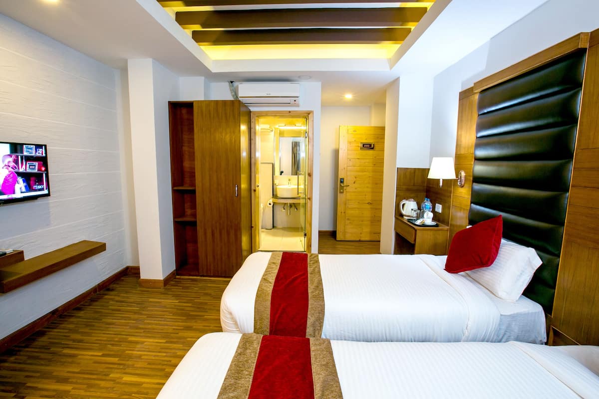 A hotel room with two beds, a TV, a wooden floor, and a bathroom visible through an open door.