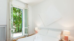 Quarto de hotel com uma cama, duas mesas de cabeceira com luminárias, uma janela com cortinas e vista para o verde lá fora.
