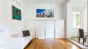 Uma sala de estar moderna com um sofá branco, uma mesa de centro redonda e uma pintura de paisagem urbana na parede.