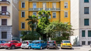Um edifício amarelo com várias varandas e carros estacionados na frente.