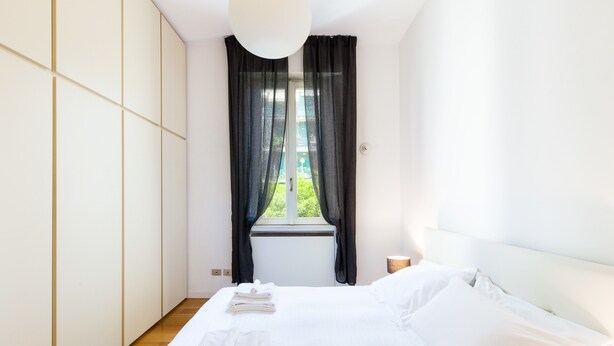 Quarto de hotel com uma cama grande, uma janela com cortinas leves e vista para o verde lá fora.