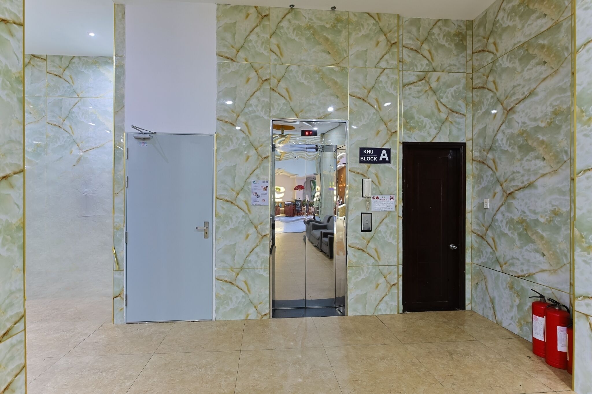 An elevator with a marble wall design, a fire extinguisher, and a sign indicating the direction to the hotel block A.