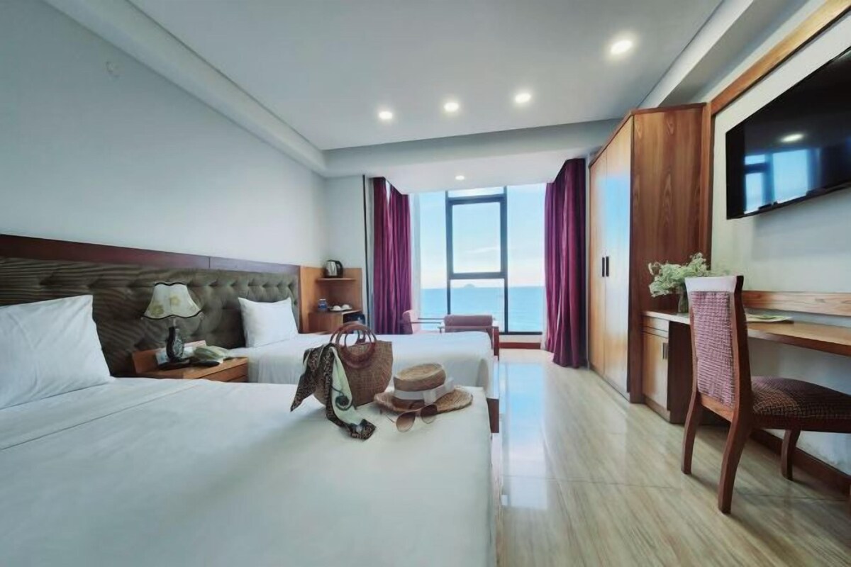 Habitación de hotel con una cama grande, un escritorio, una silla, un televisor y vistas al mar.