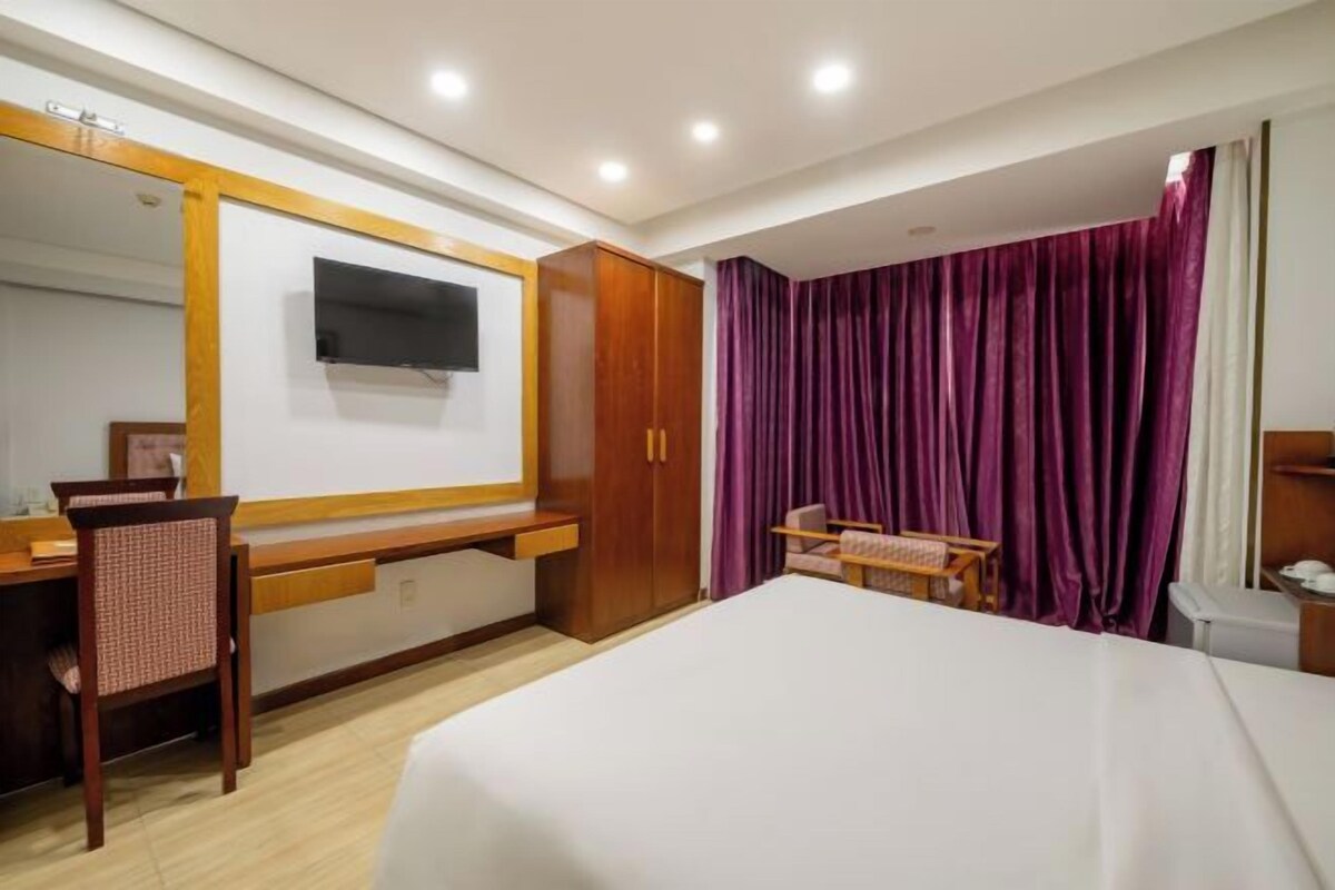 Habitación de hotel con cama, escritorio, silla, armario y televisor montado en la pared.