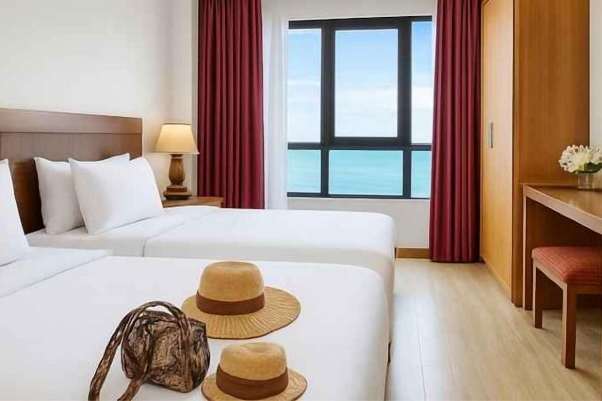 Habitación de hotel con dos camas, un escritorio y vista al mar.