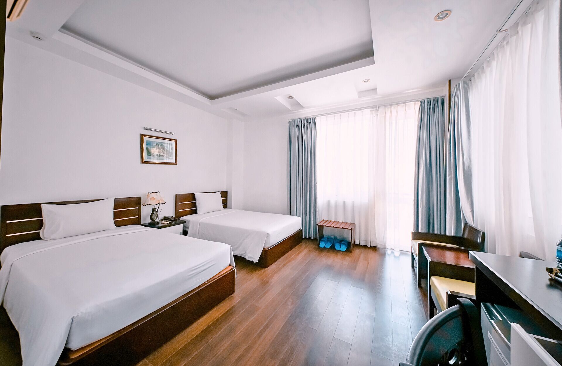 A hotel room with two beds, a desk, a chair, a small table, and a window with curtains.
