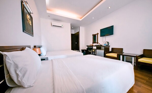 A hotel room with a large bed, a desk, a chair, a TV, and an air conditioning unit.