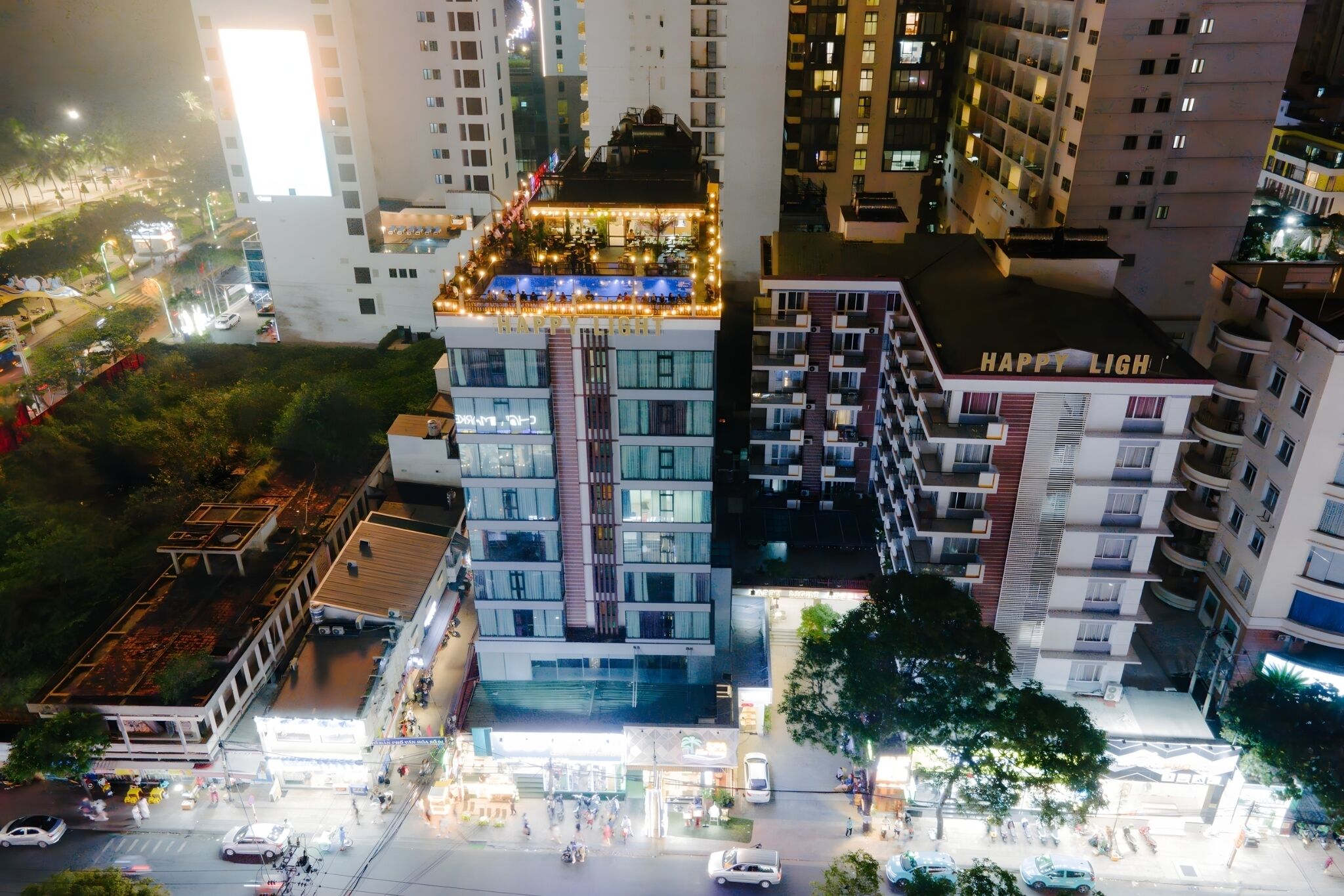 A multi-story building with a rooftop terrace decorated with lights and a sign that reads "HAPPY LIGH".